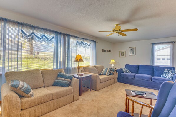 A living room with beige and blue furniture, a ceiling fan, and a view of the outdoors through large windows.