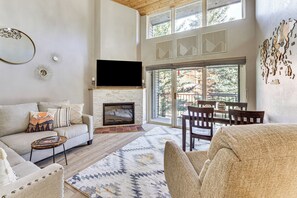 A living room with a fireplace, a sofa, a coffee table, and a TV mounted on the wall. - Walk to Angel Fire Lifts! Skier-Friendly Mtn Condo (Angel Fire)