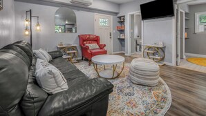 Ein Wohnzimmer mit einer Ledersofa, einem roten Sessel, einem runden Tisch und einem an der Wand befestigten Fernseher.
