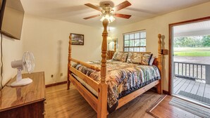 A bedroom with a wooden bed, a ceiling fan, a fan on a wooden table, and a view of the outdoors through a glass door. - Fisherman's Paradise! Lake Talquin Townhome (Quincy)