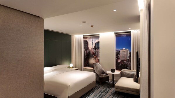 A hotel room with a large bed, a chair, a small table, and a view of a cityscape through a window. - Doubletree By Hilton Auckland Albert Street (Auckland)