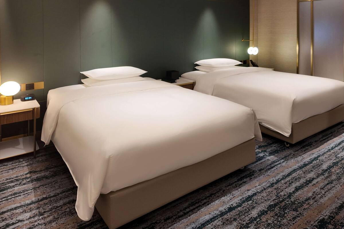 A hotel room with two beds, a nightstand with a lamp, and a carpeted floor.