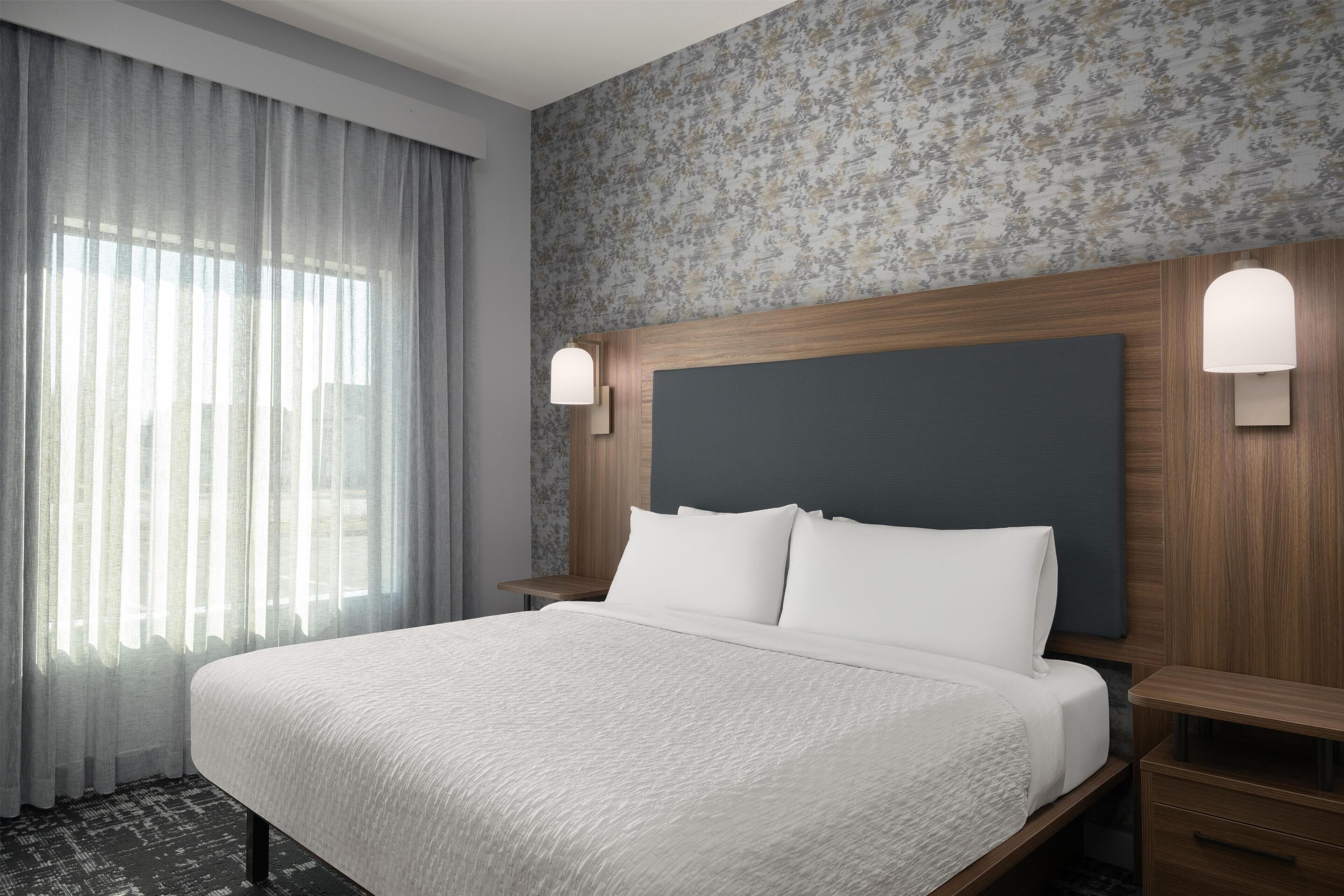 A hotel room with a large bed, a wooden headboard, two bedside tables, and a floral-patterned wall.