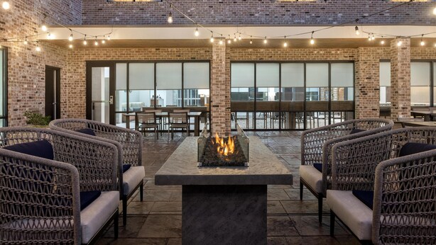 An outdoor seating area with wicker chairs, a central fire feature, and string lights. - Homewood Suites By Hilton Covington, Ga (Covington)