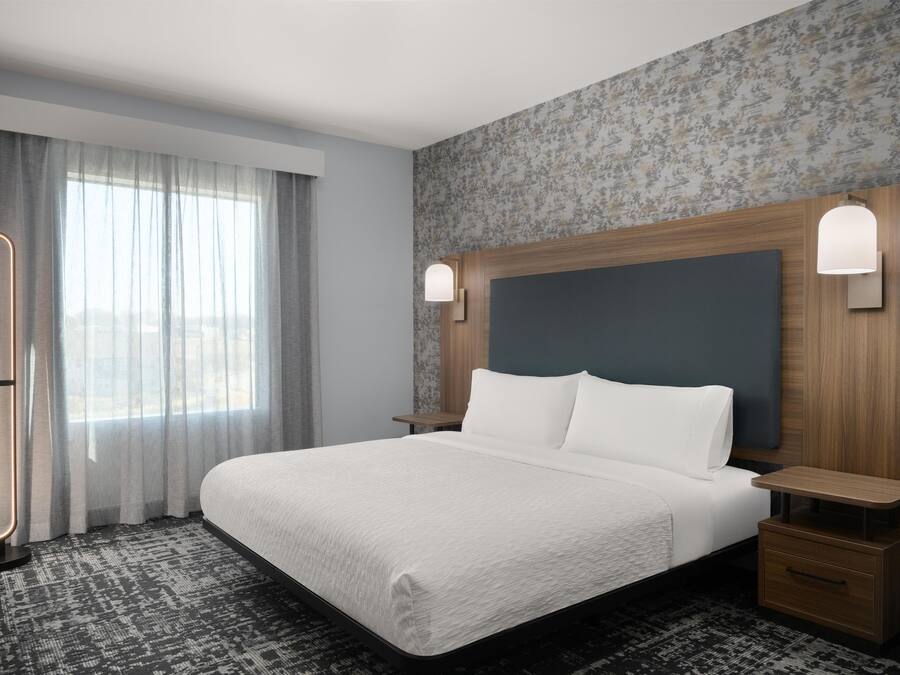 A hotel room with a large bed, a nightstand, a lamp, and a window with curtains.