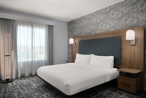 Habitación de hotel con una cama grande, una mesita de noche, una lámpara y un ventanal con cortinas.