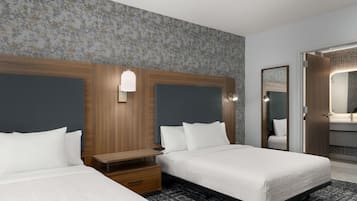Una habitación de hotel con dos camas, una mesita de noche, un espejo y un baño con lavamanos y espejo.