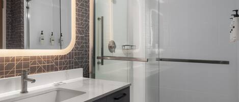 Une salle de bain moderne dotée d’une douche à parois de verre, d’un meuble-lavabo et d’un miroir agrémenté d’un pare-splash aux motifs géométriques.