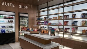 A suite shop with a refrigerated display, shelves stocked with snacks, and a wooden counter. - Homewood Suites By Hilton Covington, Ga (Covington)