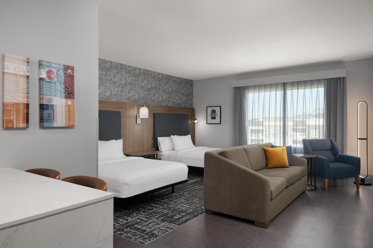 A hotel room with two beds, a sofa, a desk, and a chair.