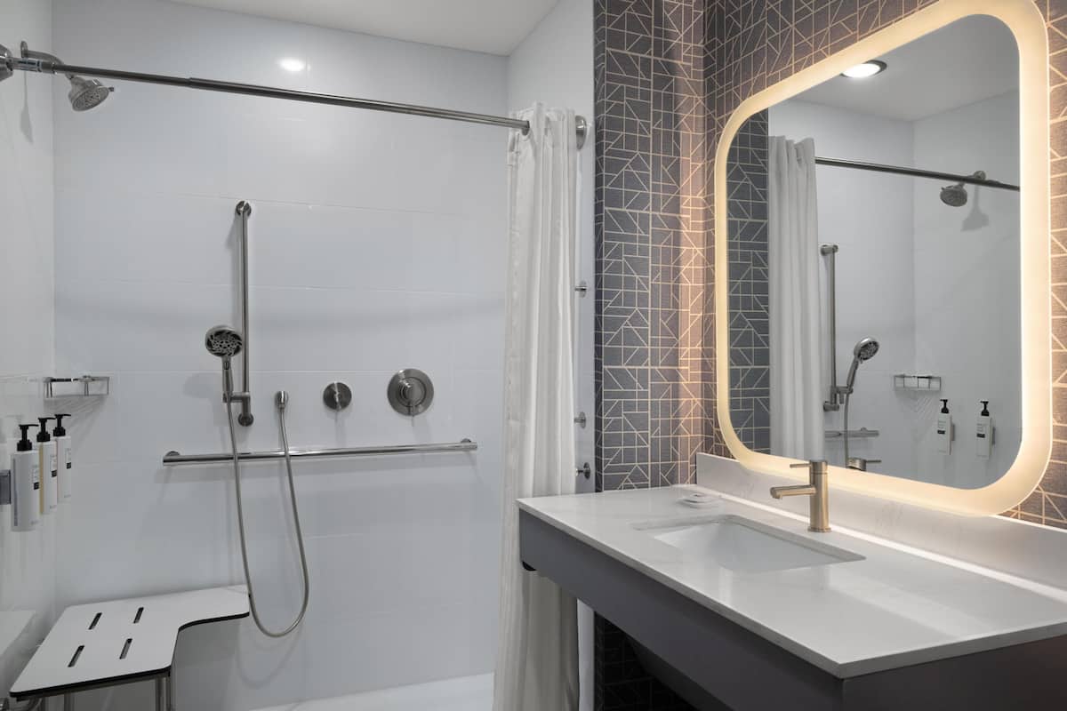 A modern bathroom with a shower, a vanity with a large mirror, and a towel rack.