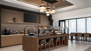A modern kitchen area with a central island, bar stools, and a television mounted on the wall. - Homewood Suites By Hilton Covington, Ga (Covington)