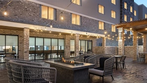 An outdoor patio with wicker furniture, a central fire feature, and string lights. - Homewood Suites By Hilton Covington, Ga (Covington)