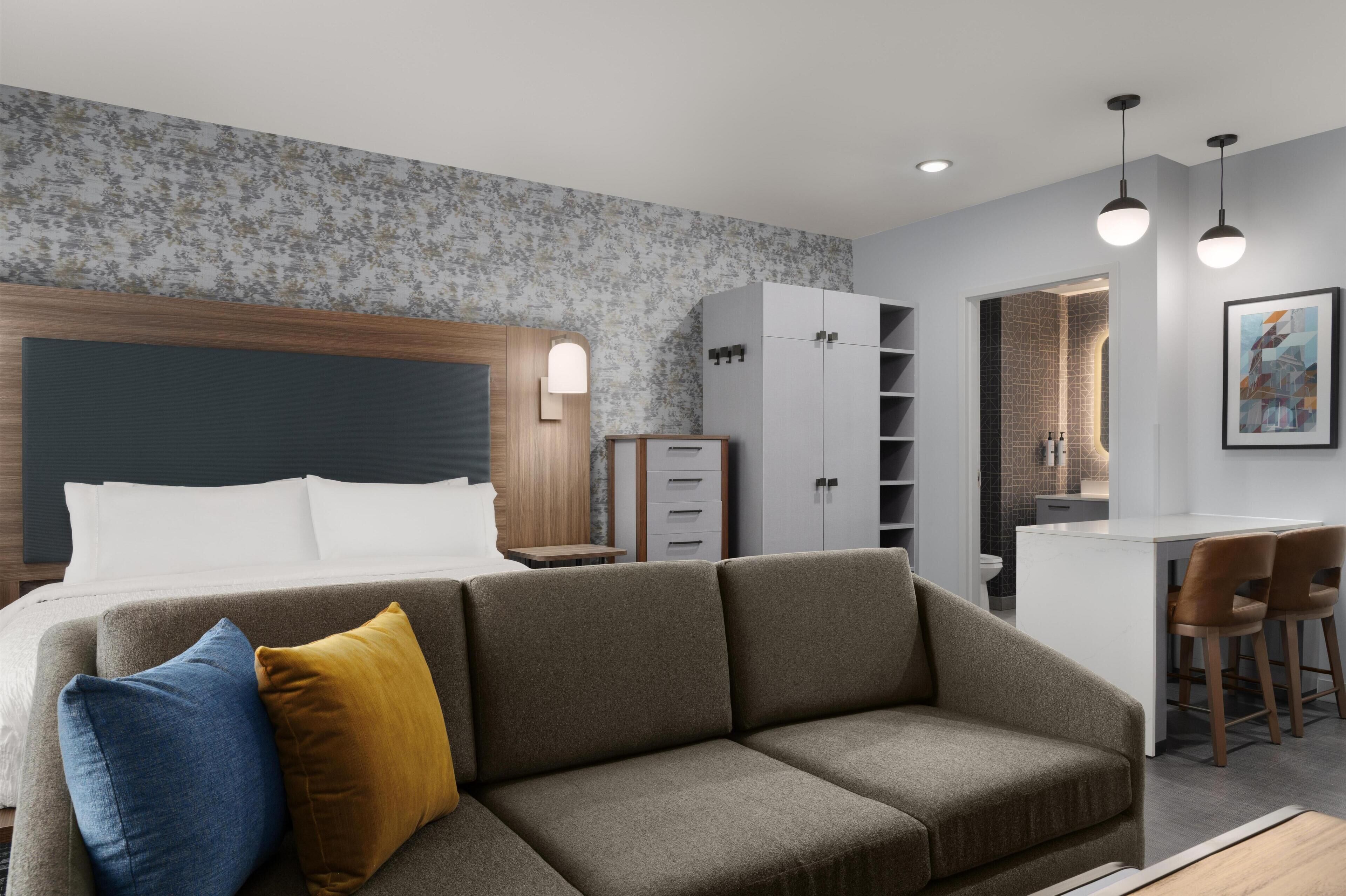 Una habitación de hotel moderna con sofá, cama, escritorio y kitchenette.