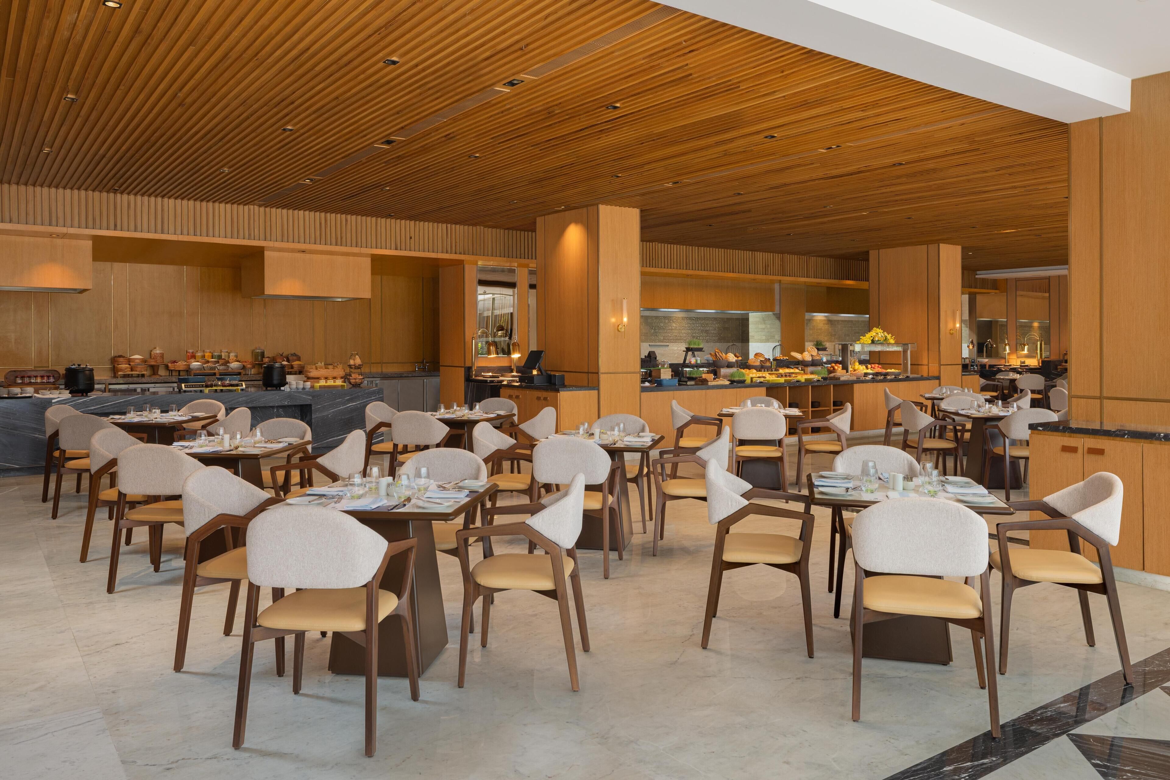 A modern dining area with wooden ceiling panels, marble flooring, and contemporary furniture.