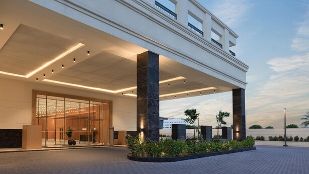 Une entrée d’hôtel moderne, dotée d’une allée couverte, de grandes portes vitrées et d’un espace paysager agrémenté de plantes.