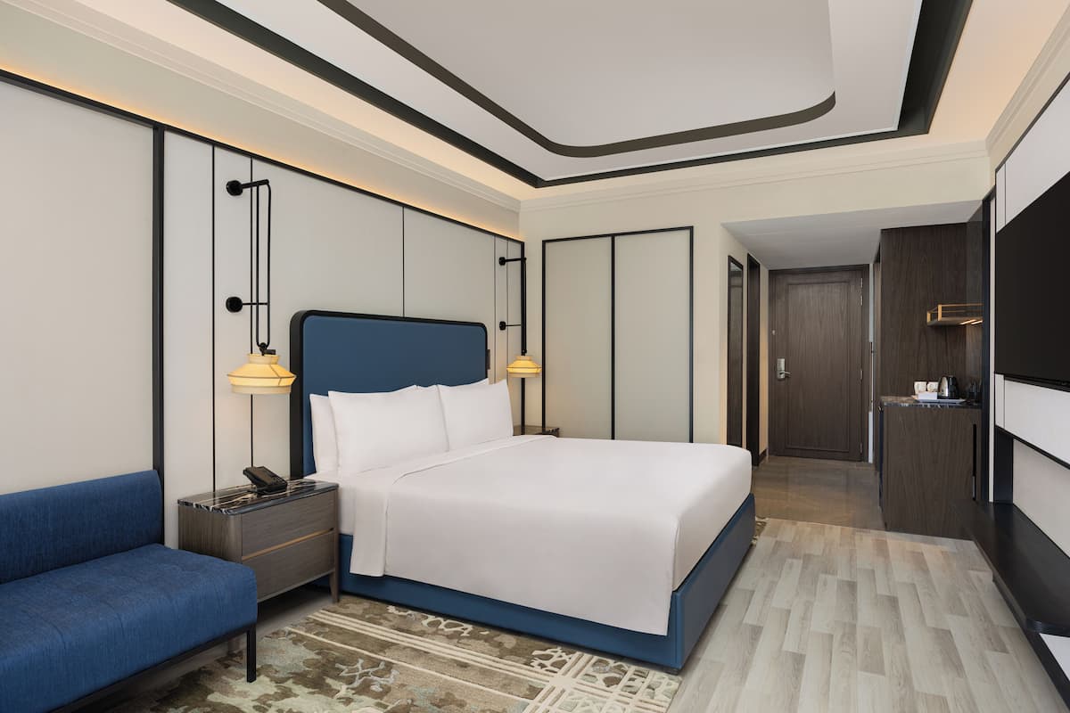 Een moderne hotelkamer met een groot bed, een nachtkastje met een lamp, een blauwe bank en een houten garderobe.