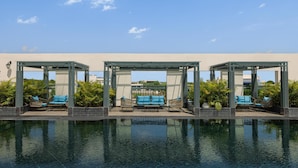 Un espace piscine comprenant trois zones de repos abritées, chacune équipée d’un banc et d’une chaise.
