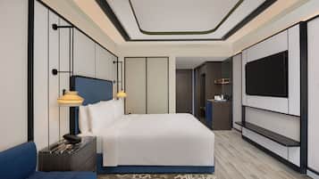 A modern hotel room with a large bed, a TV mounted on the wall, a bedside table with a lamp, and a blue sofa.