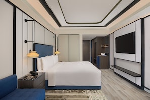 A modern hotel room with a large bed, a TV mounted on the wall, a bedside table with a lamp, and a blue sofa. - Doubletree by Hilton Bengaluru Airport (Bengaluru)