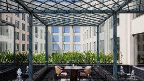 Un espace extérieur aménagé, abrité et doté de tables et de chaises, entouré d’éléments décoratifs aquatiques et de plantes.