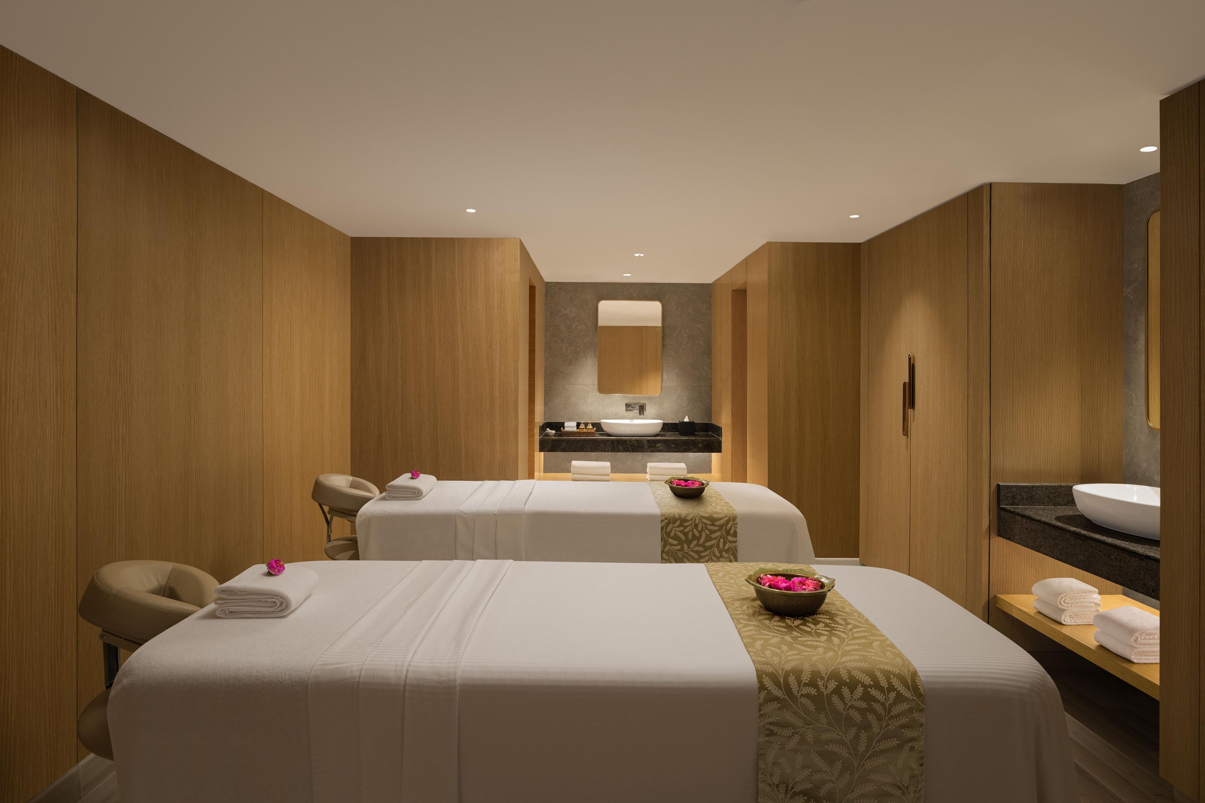 A hotel room with two beds, a bathroom with a large mirror, and a reception desk.