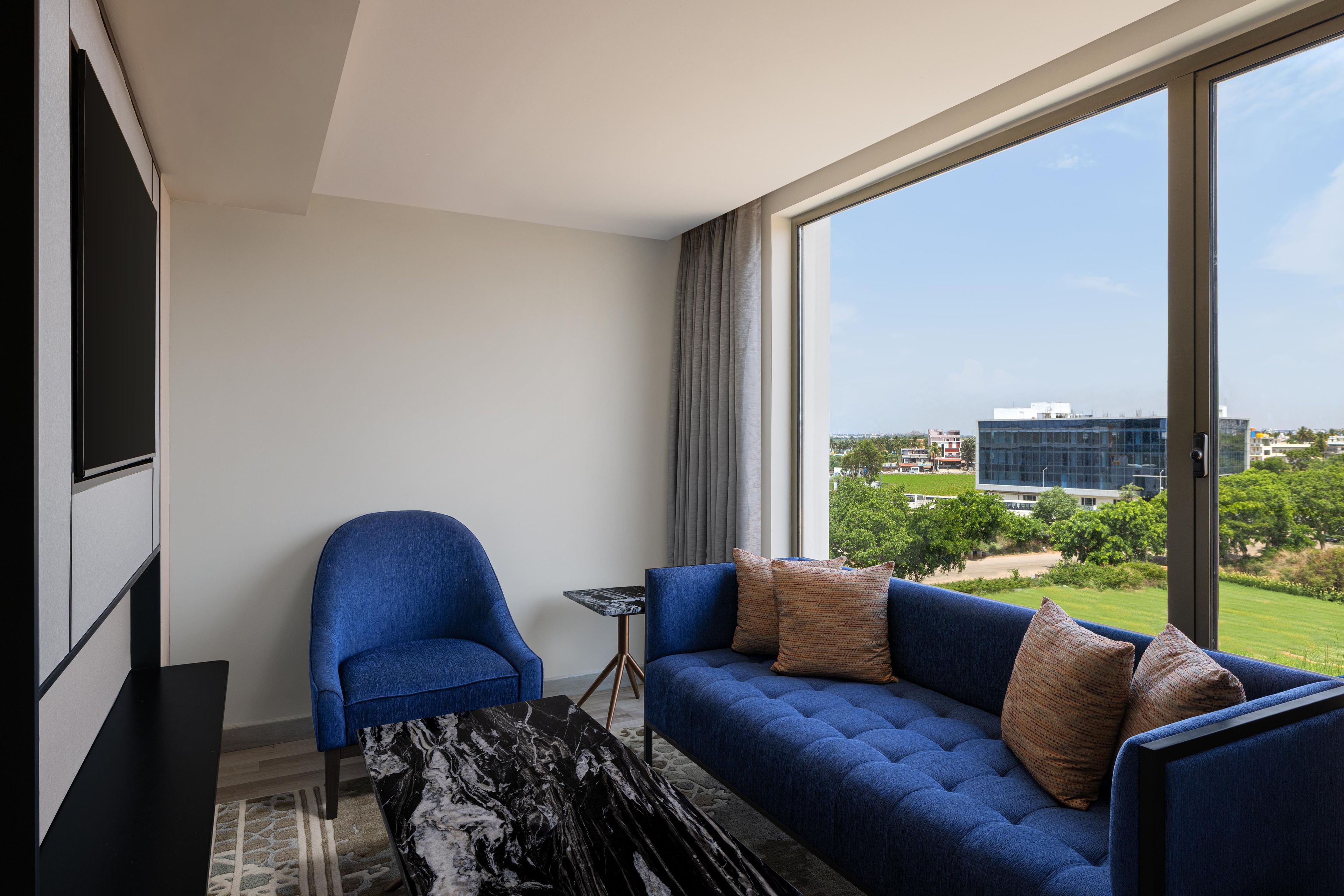 A modern room with a blue sofa, a blue armchair, a small table, and a large window offering a city view.