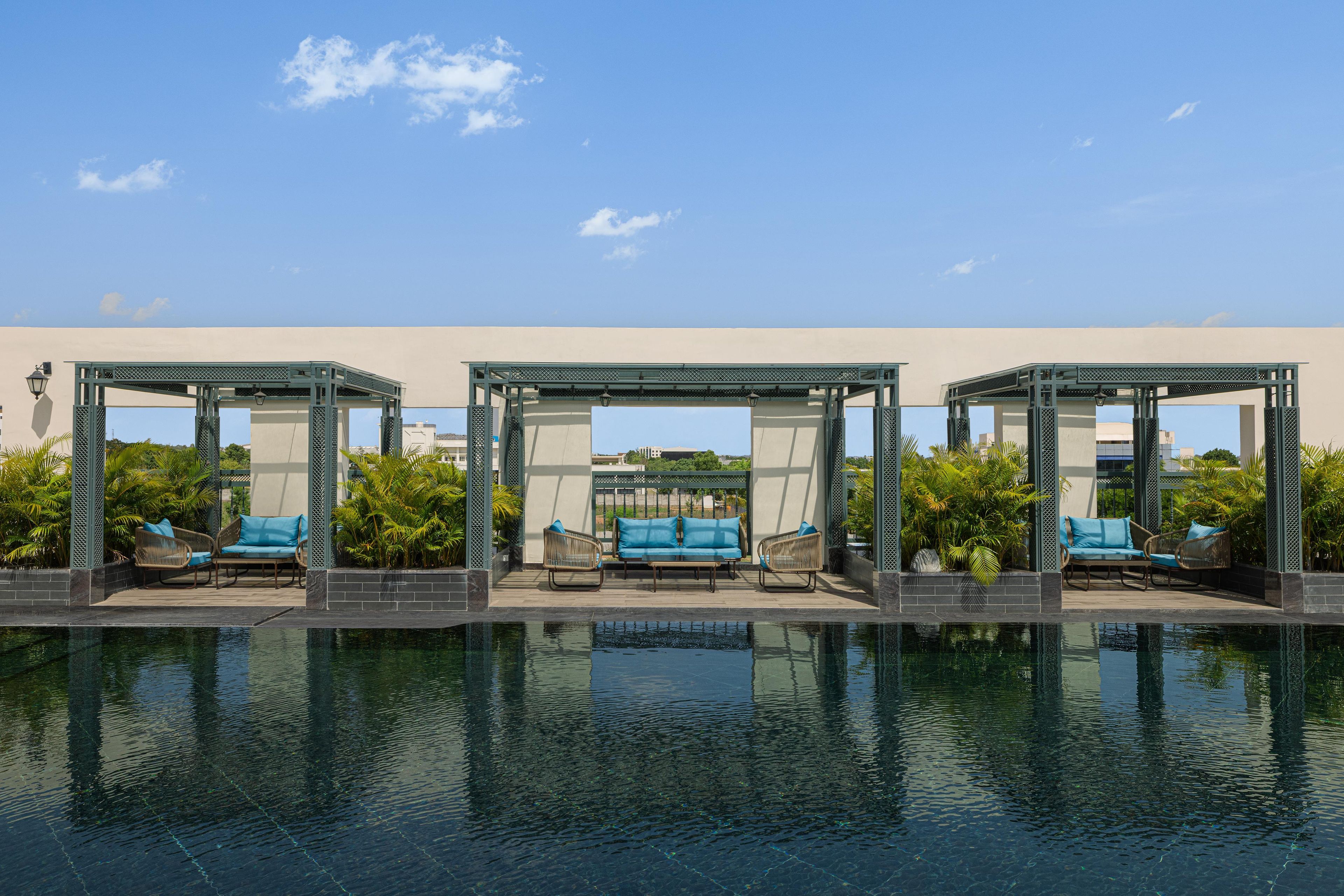 A pool area with three covered seating areas, each with a bench and a chair.