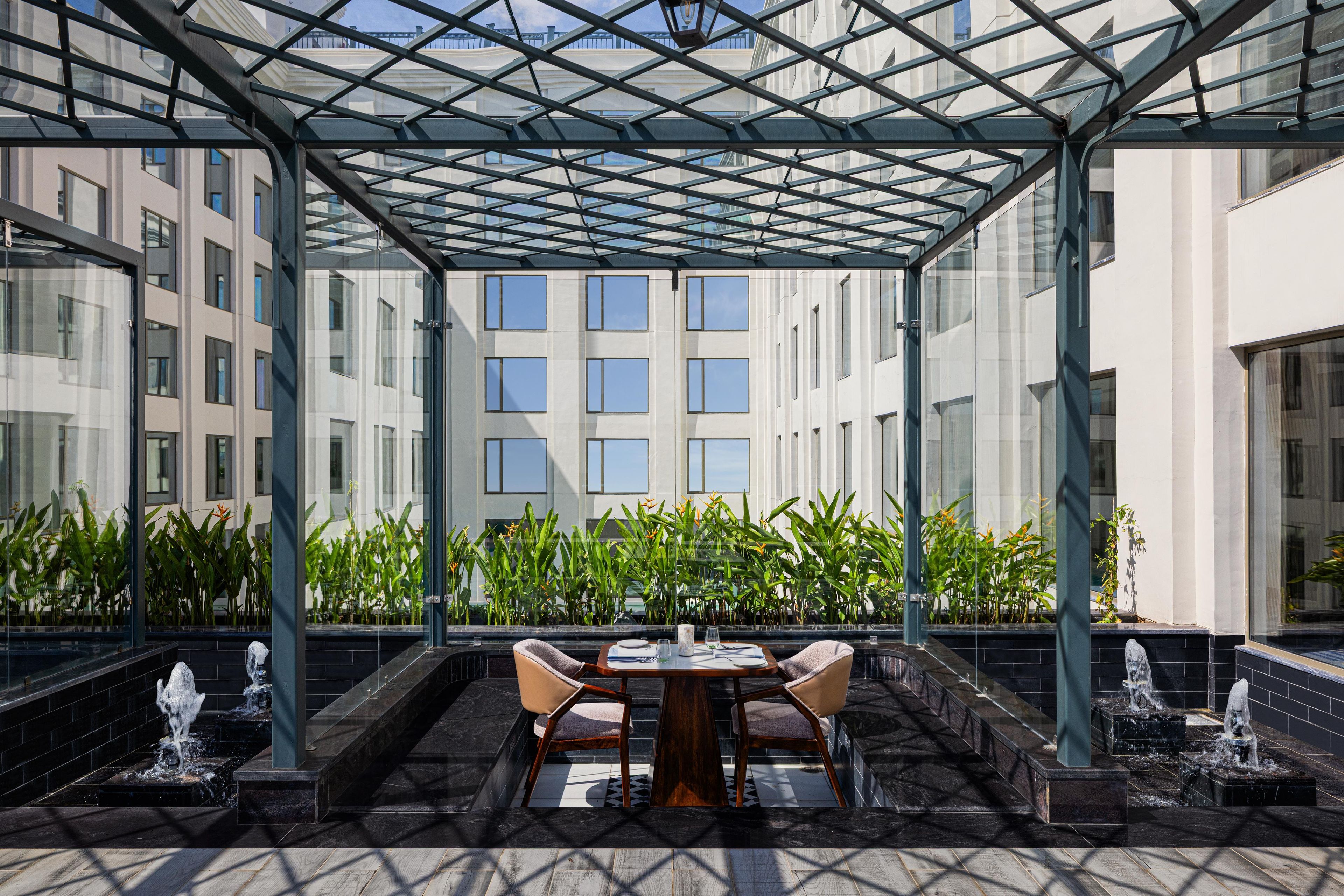 A covered outdoor seating area with a table and chairs, surrounded by water features and plants.