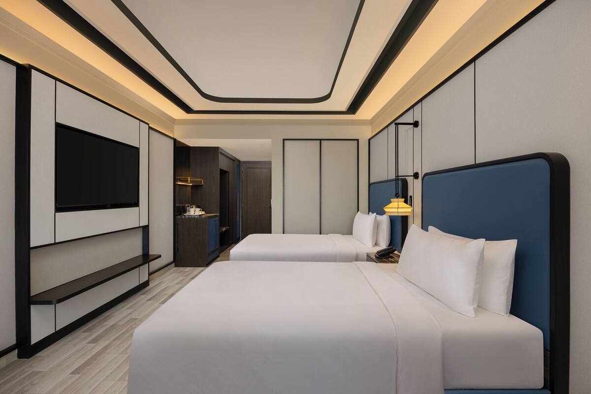 Een moderne hotelkamer met twee bedden, een televisie en een minibar.
