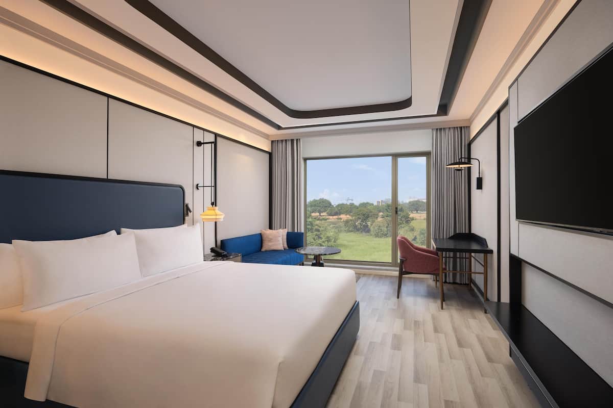 Een hotelkamer met een groot bed, een bank, een kleine tafel, een televisie en een groot raam met uitzicht.
