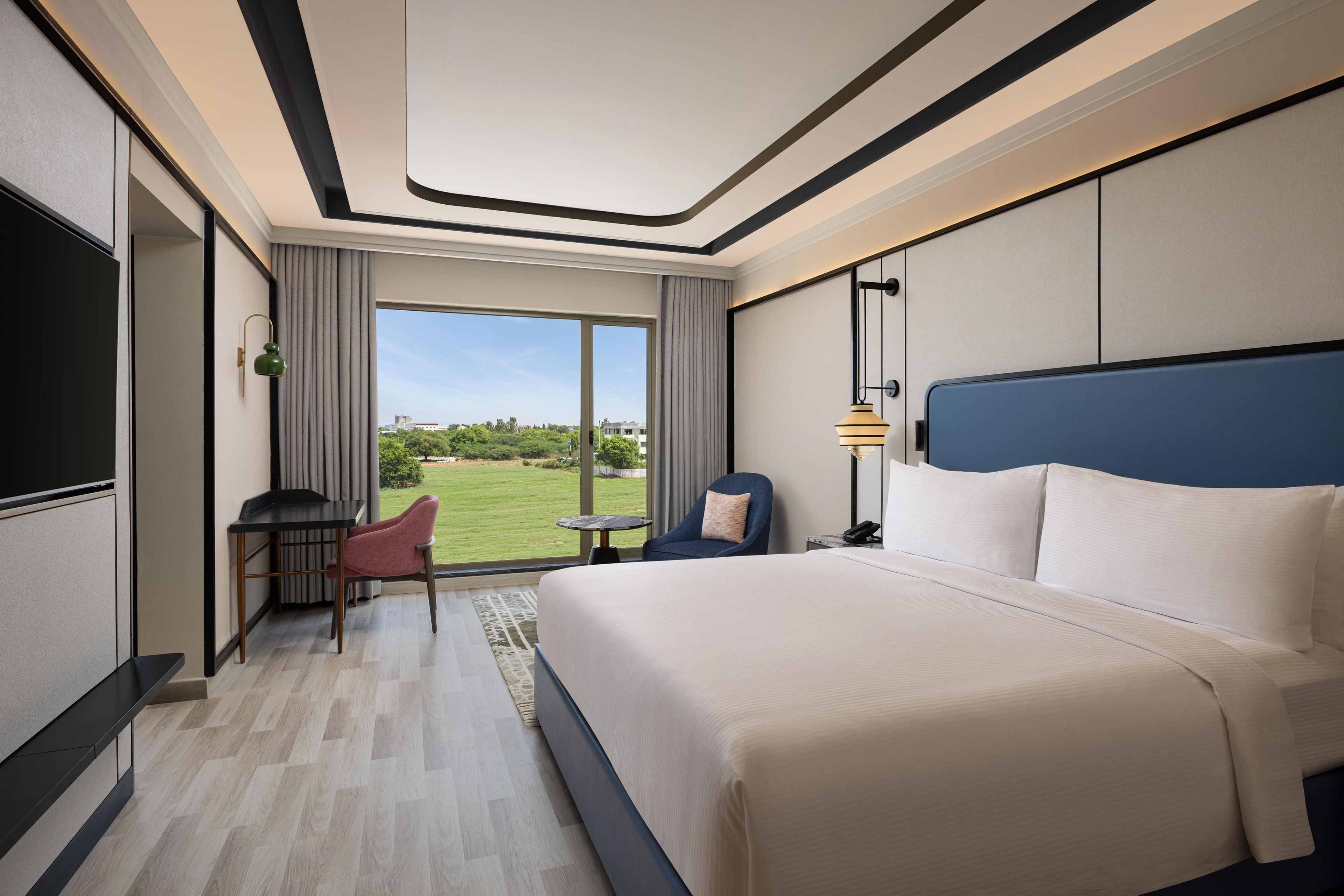 A hotel room with a large bed, a desk, a chair, a small table, and a view of the outdoors.