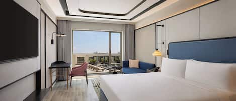 A modern hotel room with a large bed, a desk, a chair, and a view of the outdoors.