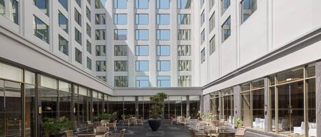 Un moderno atrio de hotel con una zona de estar central, ventanas amplias y una fachada de edificio simétrica.