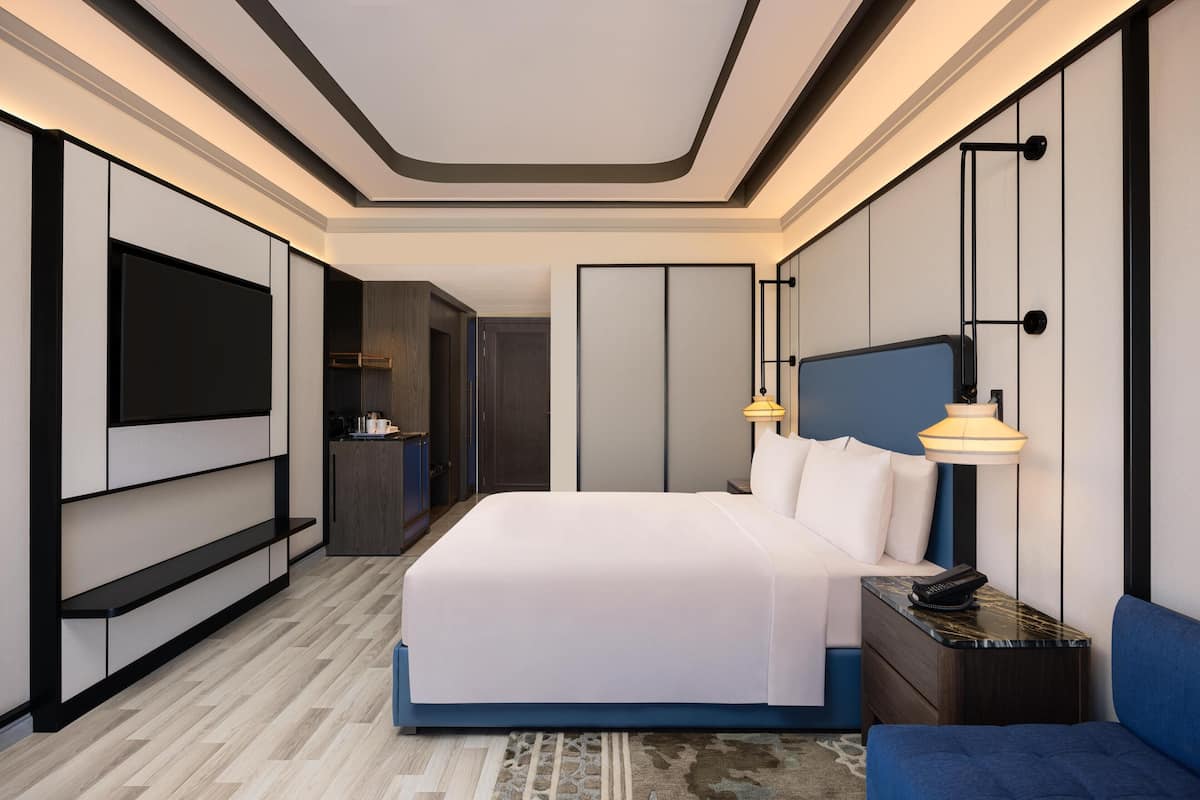 A modern hotel room with a large bed, bedside tables, a TV, and a desk area.