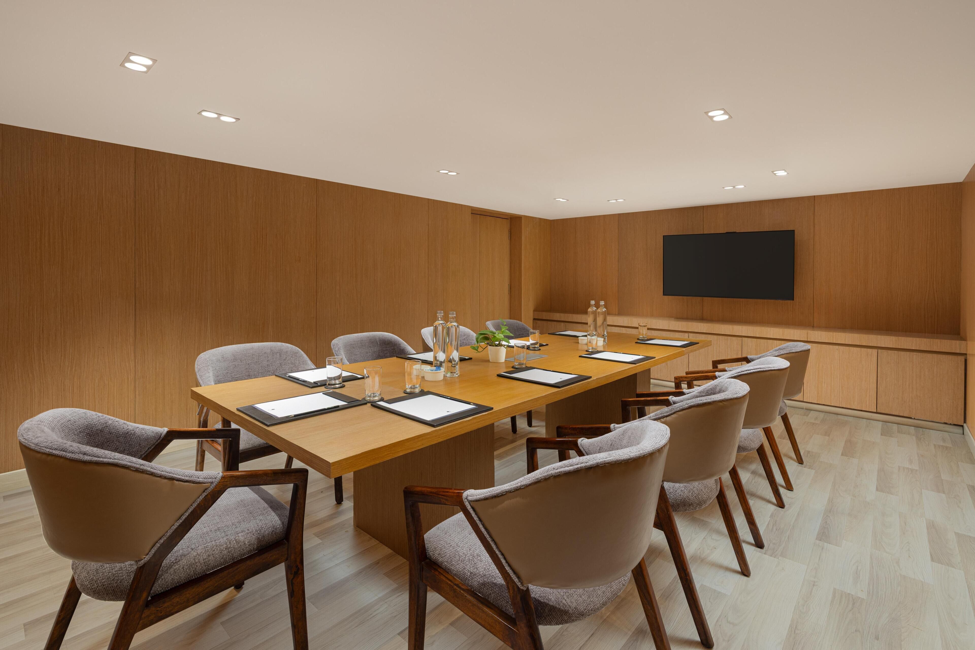 A conference room with a long table, chairs, a flat-screen TV, and recessed ceiling lights.