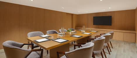 A conference room with a long table, chairs, a flat-screen TV, and recessed ceiling lights.