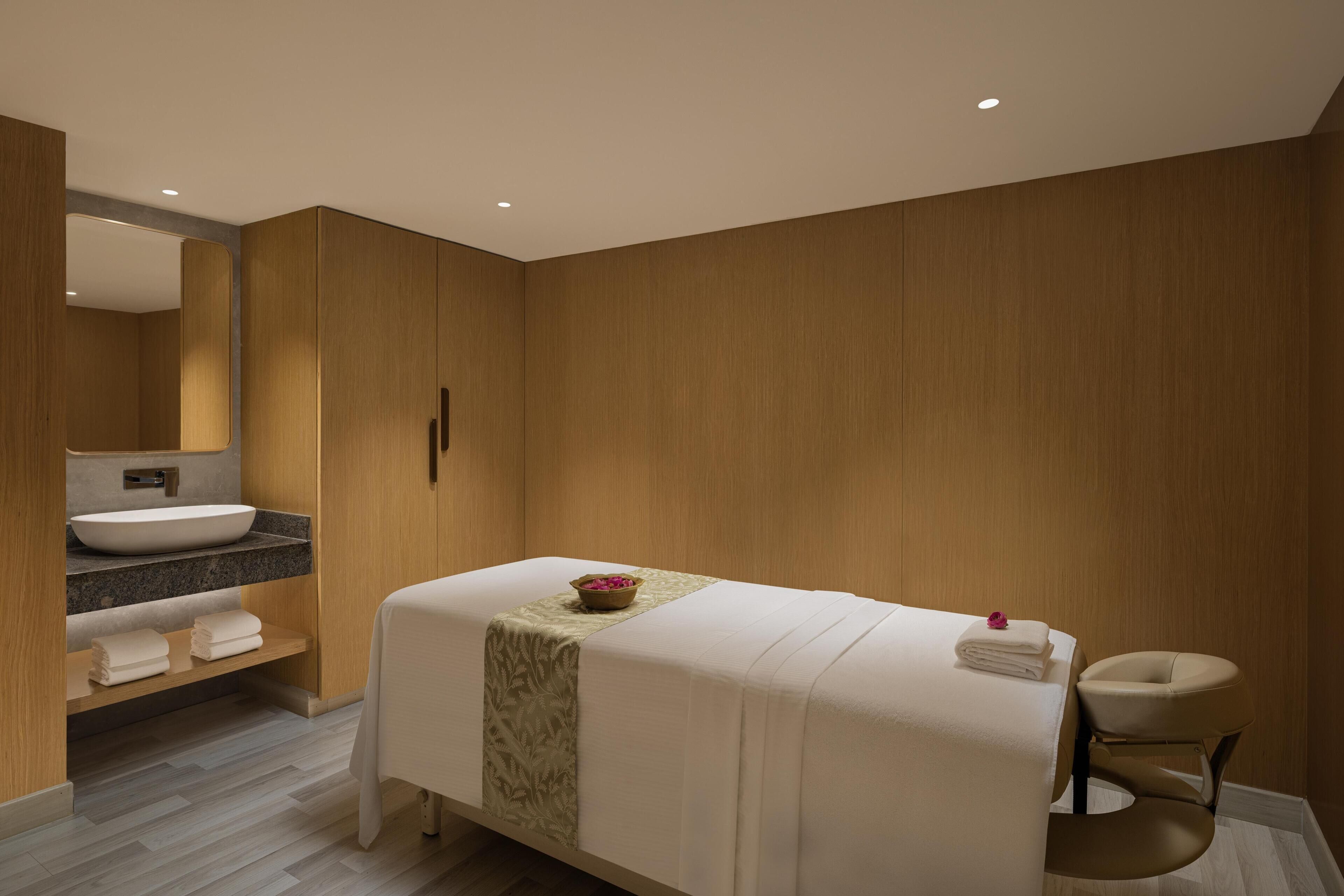 A modern bathroom with a large mirror, a sink, a towel rack, and a massage table.