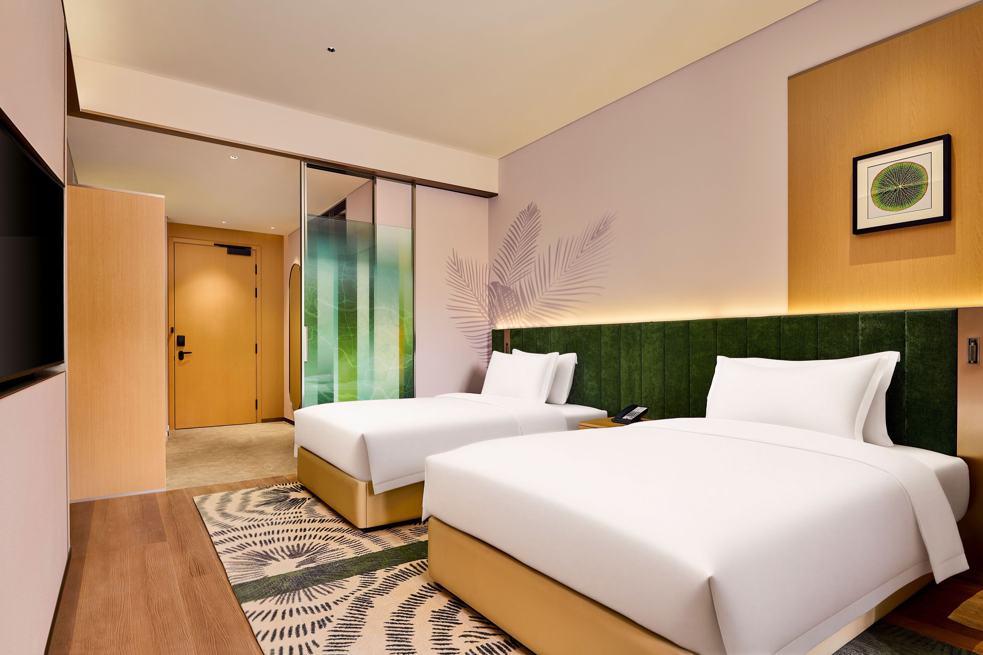 Ein Hotelzimmer mit zwei Betten, einem grünen Kopfteil, einem großen Spiegel und einem gerahmten Bild an der Wand.