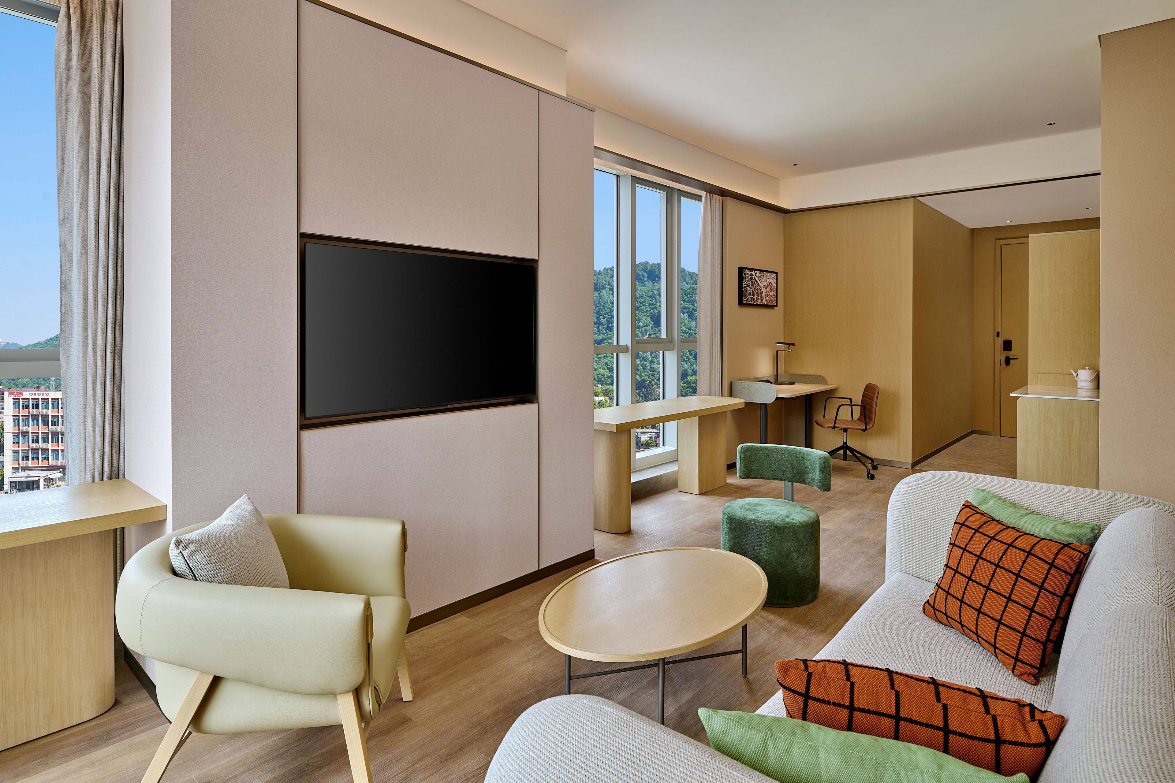 A modern hotel room with a flat-screen TV, a sofa, a small table, and a view of the outdoors.