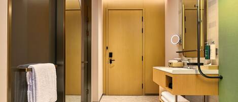 A modern bathroom with a wooden door, a glass shower enclosure, a marble countertop, and a mirror with a ring light.