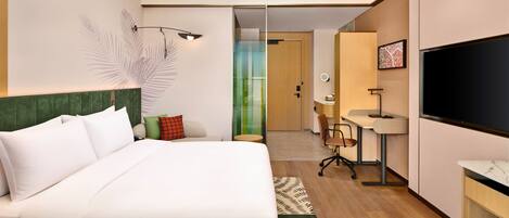 A hotel room with a bed, a desk, a TV, and a bathroom visible through a glass door.