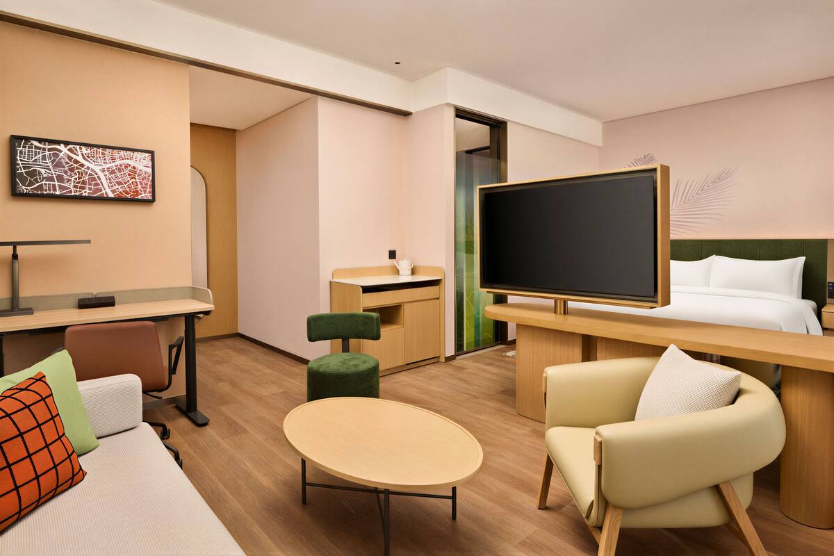 A hotel room with a bed, a desk, a chair, a small table, and a television.