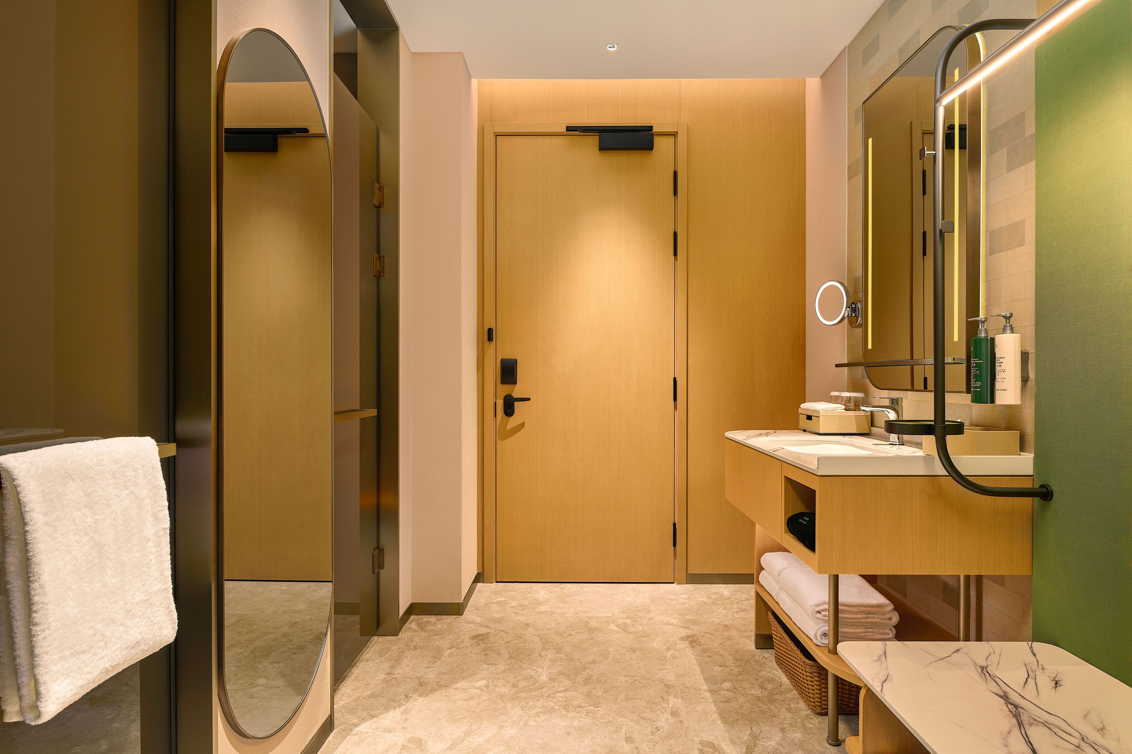 A modern bathroom with a wooden door, a round mirror, a sink, and a bench.