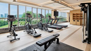 Una palestra con tapis roulant, ellittiche, una panca e una rastremazione, con ampie finestre che offrono vista sulla città.