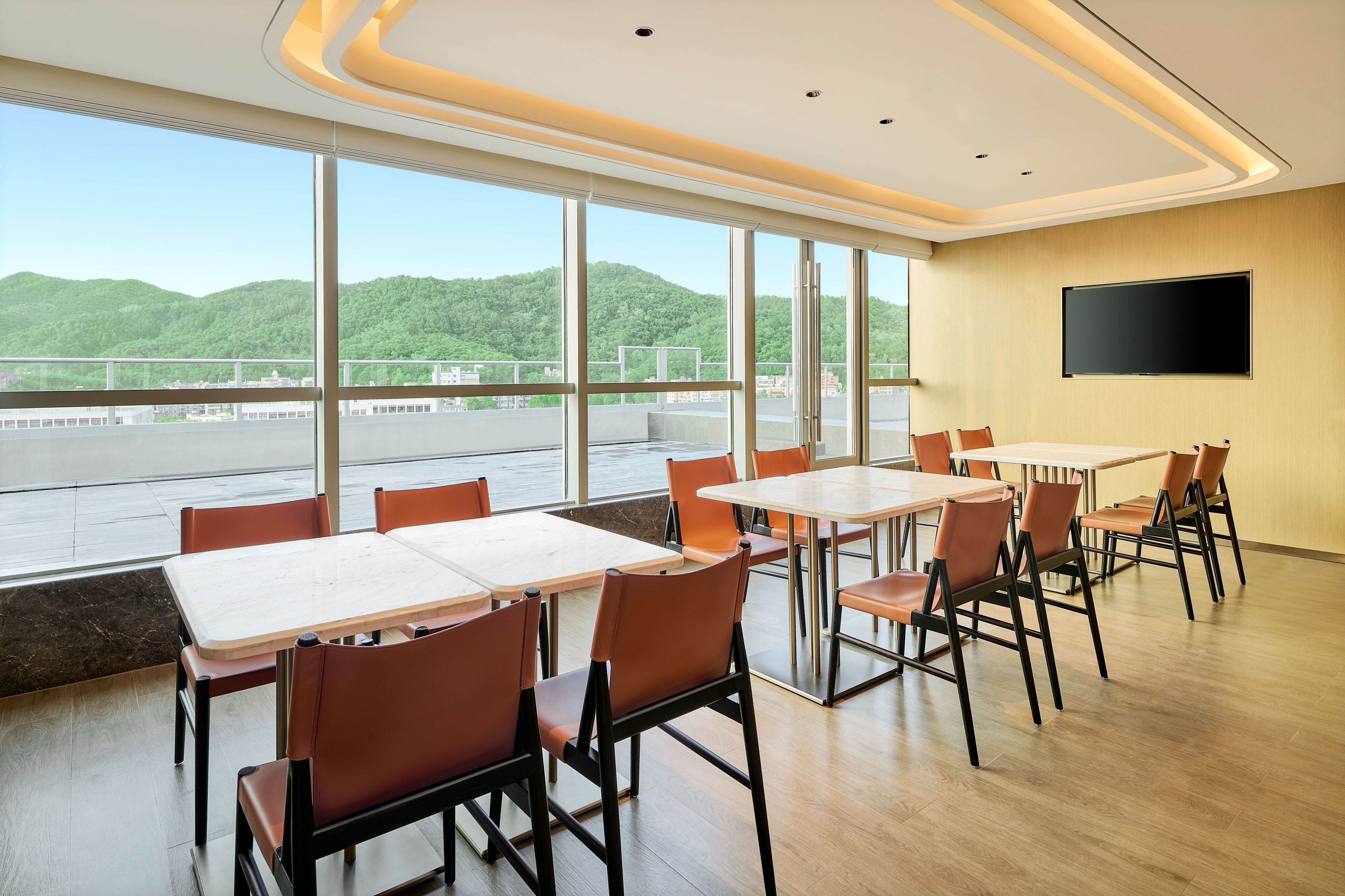 A conference room with large windows, a flat-screen TV, and a view of a green landscape.