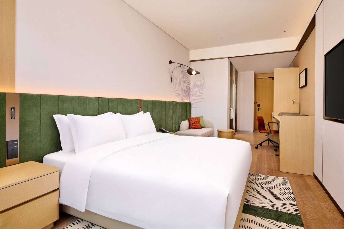 A modern hotel room with a large bed, a desk, and a chair.