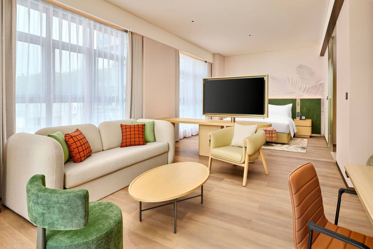 A hotel room with a sofa, a small table, a TV, a bed, and a chair.