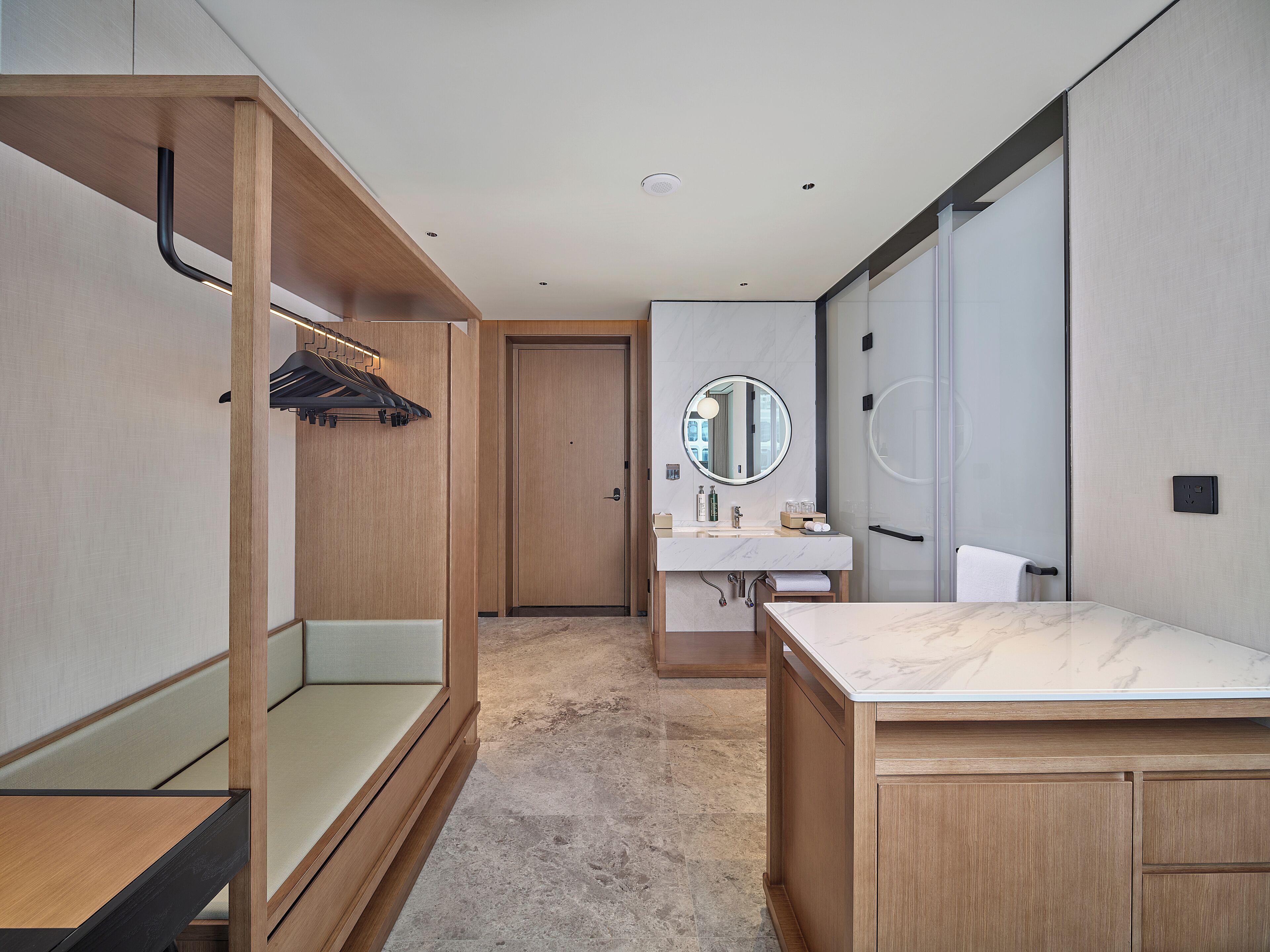 A modern bathroom with a wooden vanity, a round mirror, and a towel rack.
