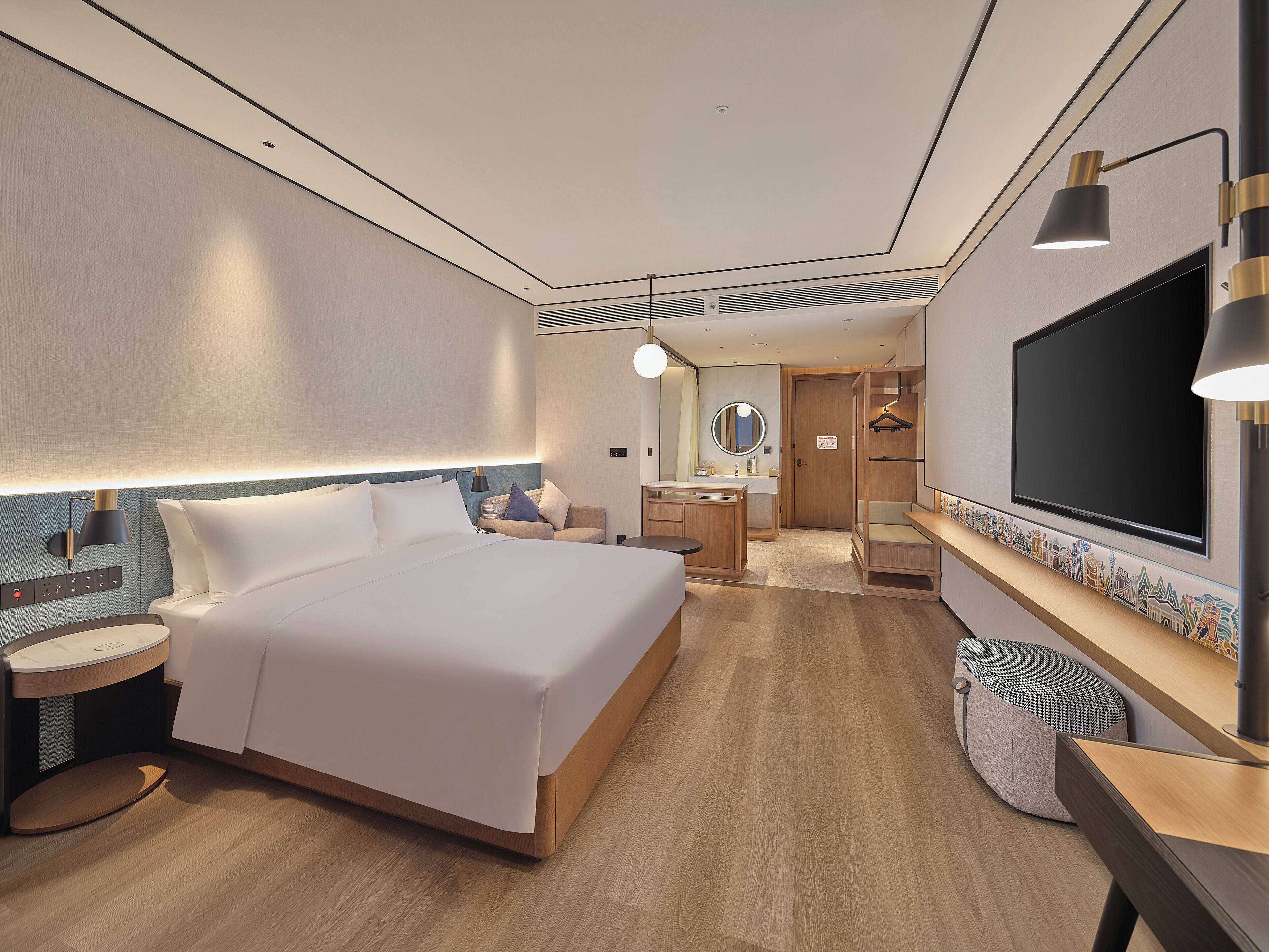 A modern hotel room with a large bed, bedside tables, a desk, a mirror, and a TV.